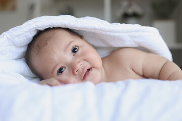 Adorable baby crawling on the bed, body covered by the blanket. Happy moments.