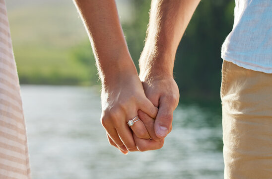 Holding hands, engagement and couple at lake outdoors for love, trust and support. Commitment, care and ring jewelry of woman and man together for romance, bonding or affection with soulmate at creek