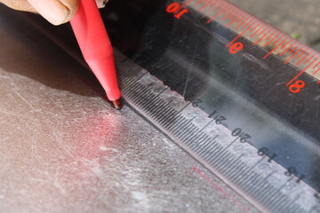 A worker drawing straight line on metal sheet with ruler and marker
