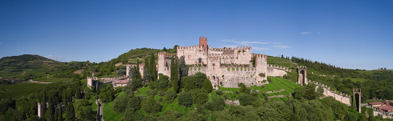Fototapeta na wymiar Panoramic view of Soave castle surrounded by vineyard plantations. Soave castle aerial view Verona province, Italy. Ancient castle on a hill in Italy. Italian flag on the main tower of Soave Castle.