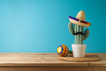 Mexican party concept with cactus, maracas and sombrero hat on wooden table over blue background. Cinco de Mayo holiday celebration