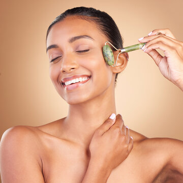Facial, massage and skincare with a model woman in studio on a brown background for natural antiaging beauty. Wellness, luxury and product with an attractive young female using a roller for skin lift