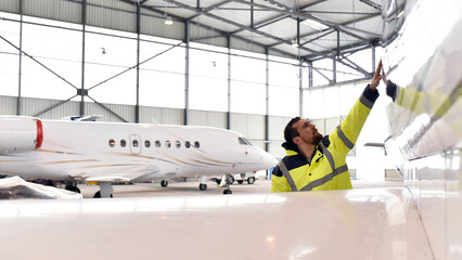 Aircraft mechanic inspects and checks the technology of a jet in a hangar at the airport - 584609447