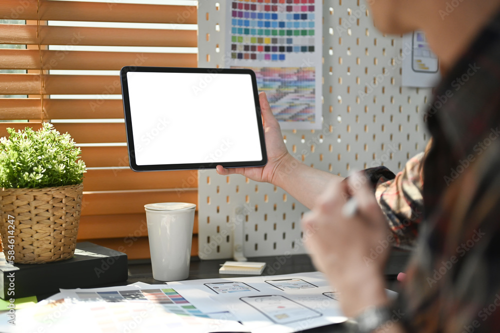 Poster back view of young creative man sitting at workplace and using digital tablet. empty screen for grap