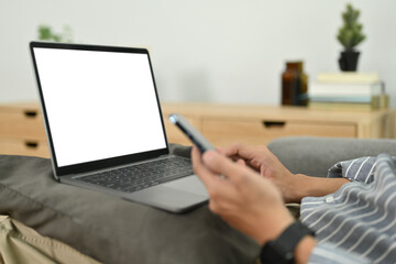 Cropped image of man sitting on couch with laptop and chatting on mobile phone. People. technology and communication concept