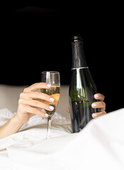 hands of a woman lying in bed with a glass and a bottle of champagne, celebrations and morning concept, hangover and bad after parties, hangover tips