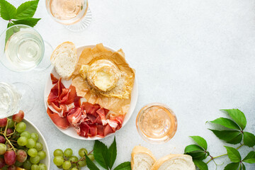 Top view of table with rose and white wine in glasses, plates with grapes, cheese and jamon, baked...