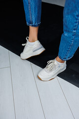 Sports shoes for women. Slender female legs in jeans and white stylish casual sneakers. Women's comfortable summer shoes. Casual women's fashion