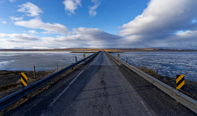 Fototapeta premium Pont de bitume et de gravier traversant un fjord en Islande recouvert par la glace et la neige 