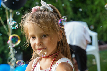 Portrait of a blonde girl in soap bubbles. Children's party in the backyard. Summer entertainment