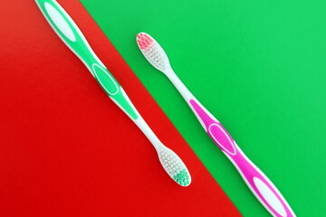 Two toothbrushes of different colors lie on a red and green background.