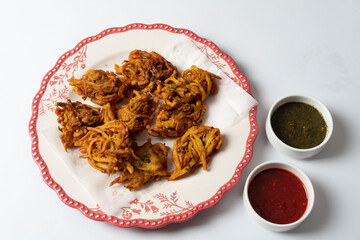 Fried onion pakora favourite Indian-pakistani Tea-Time snack during the rainy season. served with mint and sweet chilli sauces on textured background