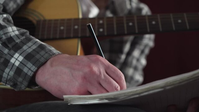 young man writing song lyrics with acoustic guitar in cozy room. close-up