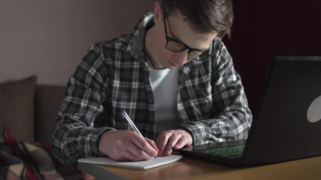 A young man notes an online lecture in a notebook. distance education. slide.