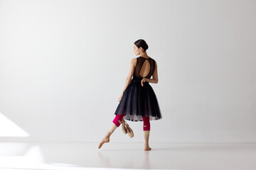 Back view. Dreaming beautiful ballerina wearing black dress posing with pointe shoes in hands over white background © Lustre Art Group 