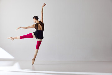 Back view. One beautiful ballerina wearing pointe shoes and demonstrating flexibility with graceful hand movements over white background © Lustre Art Group 
