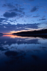 雲の浮かぶ夜明けの空と湖畔の森を湖面に映す湖。日本の北海道の屈斜路湖。