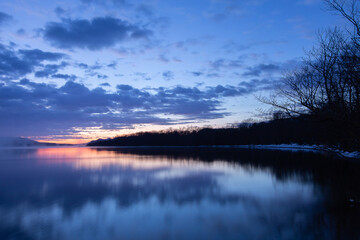 雲の浮かぶ夜明けの空と湖畔の森を湖面に映す湖。日本の北海道の屈斜路湖。