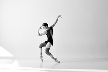 Fototapeta na wymiar Monochrome. One emotional ballerina wearing pointe shoes dancing on fingertips with hands over white and black background