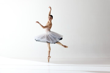 Portrait of tender young ballerina dancing, performing over white studio background. Beauty of...