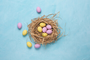 Banner for the Easter holiday. Colored eggs in a straw nest and white spring flowers on a blue background. Place for text. Top view.