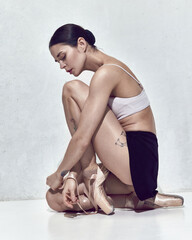Adorable young woman, ballerina sitting on floor after hard work in dance hall over white background © Lustre Art Group 