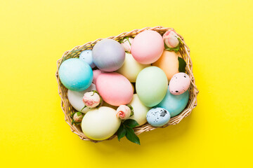 Fototapeta na wymiar Happy Easter. Easter eggs in basket on colored table with yellow roses. Natural dyed colorful eggs background top view with copy space