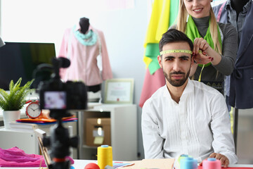 Woman seamstress stylist jokes and measures head of a male designer with centimeter.
