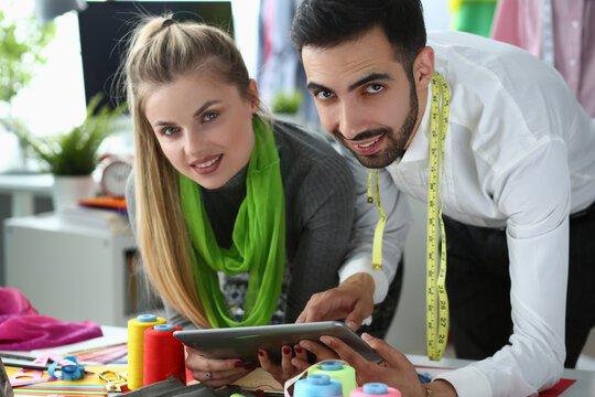 Woman and man stylist designers are holding tablet and discussing new clothes sketch