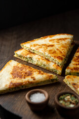 Close-up khachapuri with greens cut into pieces. Georgian flatbread with cheese and herbs served on a wooden board. Caucasian national cuisine pie