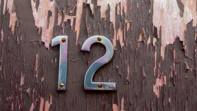 Chromed numerals depicting the number twelve on a wooden board with peeling varnish - Powered by Adobe