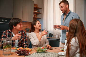 Holding glasses with water. Group of people are on the kitchen, having dinner, spending time together