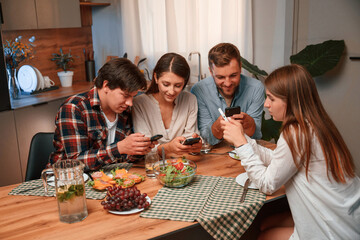 Using smartphone. Group of people are on the kitchen, having dinner, spending time together