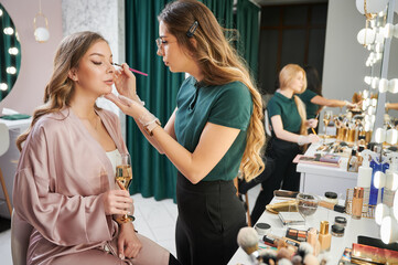 Beauty specialist applying eyeshadow on client eyelid in visage studio. Young woman sitting at...