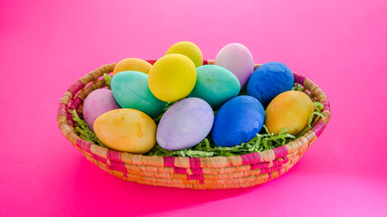 Colorful bright  Easter eggs inside basket on pink background
