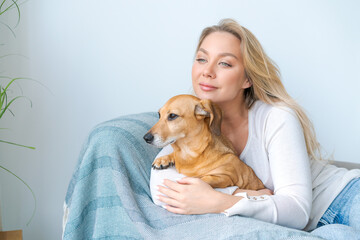 A young beautiful woman in casual clothes hugs and pets her beloved dog sitting in the bedroom of her cozy country house. Animal communication concept