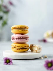 Gordijnen Stack of yellow and pink colored macaron cookies on a white marble stand. French mini dessert with almond flour. Violet flowers on grey background. Spring or summer mood. Copy space © Анна Первова