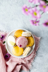 Small white plate with yellow, pink and ivory colored macaron cookies on a pink napkin. French mini...