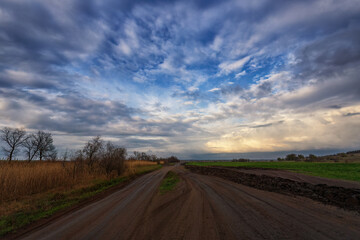 Naklejka na ściany i meble Spring country road after rain, countryside. Clouds and sky