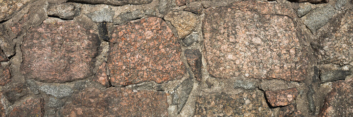 Ancient stone wall. Weathered rough surface of old masonry. Granite rock. Wall of a medieval castle. Wide panoramic texture for background and design.