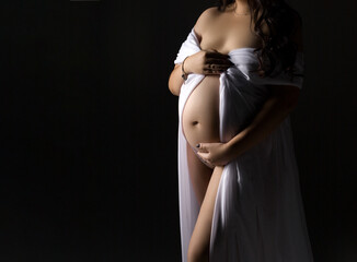 A pregnant woman in a white dress on a gray background with a place for text. Belly of a pregnant...