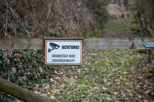 Achtung Grundstueck wird Videoueberwacht Please note that the property is under video surveillance sign attached to a wooden fence with garden in the background
