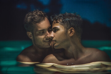 Gay couple relaxing in swimming pool at night. LGBT. Two young men kissing and hugging. Young men...