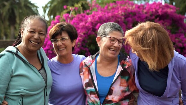 Happy multiracial senior women having fun together smiling hugging each other after sport workout at city park
