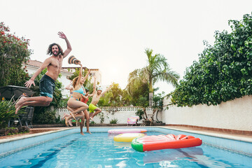 Group of happy friends jumping inside pool during summer vacations - Soft focus on left girl face -...