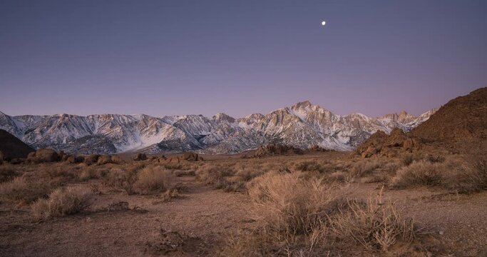 Moon Setting over snow-capped mountains as the sun rises behind the scene. High quality 4k footage
