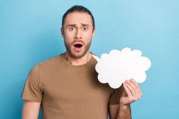 Portrait of impressed astonished guy long haircut wear khaki t-shirt hold cloud staring open mouth isolated on blue color background - obrazy, fototapety, plakaty