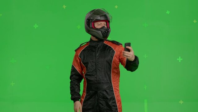 racing driver using smartphone on green screen background, portrait of sports car racer in helmet and suit, chroma key