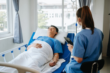 Obraz premium Friendly Female Head Nurse Making Rounds does Checkup on Patient Resting in Bed. She Checks tablet while Man Fully Recovering after Successful Surgery in hospital..