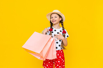 A child with paper bags from the store. Summer shopping for children. A beautiful little girl in a hat is smiling broadly.   Yellow isolated background.
